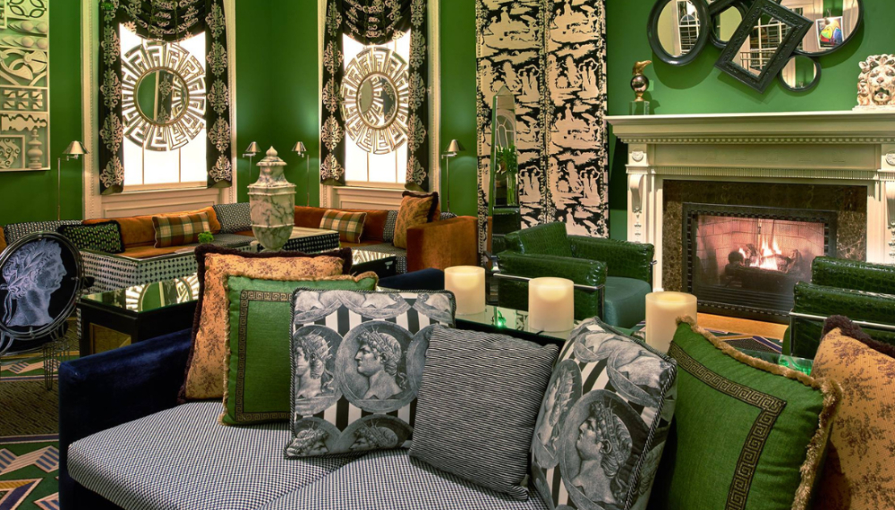 A lavish green lounge with patterned sofas, a cozy fireplace, intricate window decor, and assorted unique artworks